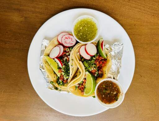Plate of tacos with salsa, lime wedges and sliced radishes.